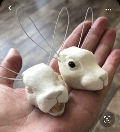 a hand holding two small white clay animals