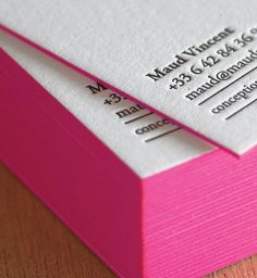 two pink and white business cards sitting on top of a wooden table next to each other