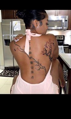 a woman with tattoos on her back is standing in front of a kitchen counter top