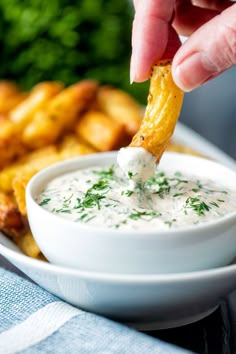 a person dipping dip into a bowl of potato wedges with parsley on top