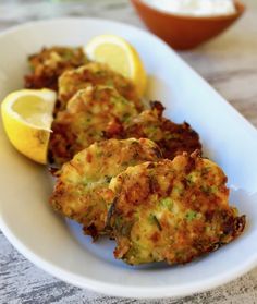 some fried food on a white plate with lemon wedges