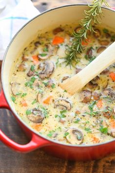 a red pot filled with mushroom soup on top of a wooden table