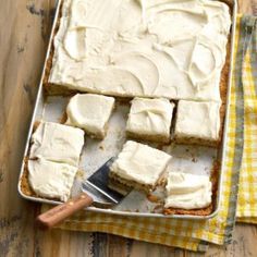 a pan filled with white frosted cake next to a yellow checkered napkin and knife