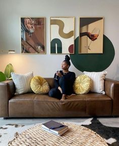 a woman sitting on a couch in front of some paintings and drinking a glass of wine