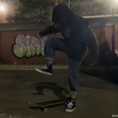 a man riding a skateboard down the side of a road at night with graffiti on the wall behind him