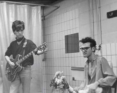 two young men playing guitars in a bathroom