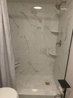 a white bathroom with marble tile and gold fixtures on the shower head, toilet, and bathtub