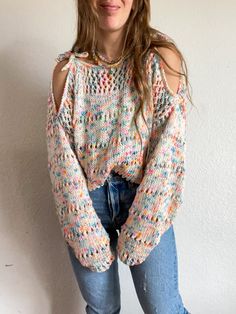 a woman standing in front of a white wall wearing ripped jeans and a colorful sweater