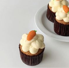 two cupcakes with frosting and carrots on them sitting on a plate