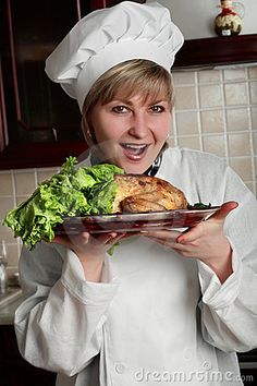 a woman in chef's outfit holding a plate with food on it and smiling at the camera