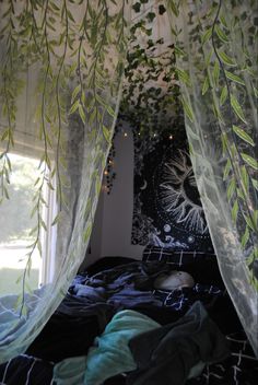 an unmade bed with sheer curtains hanging from it's sides and plants growing on the ceiling