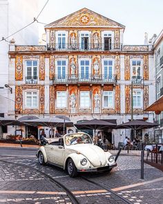 an old white car parked in front of a building with orange paint on it's side