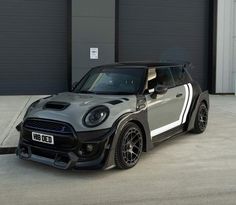 a grey and black mini car parked in front of a garage door next to a building