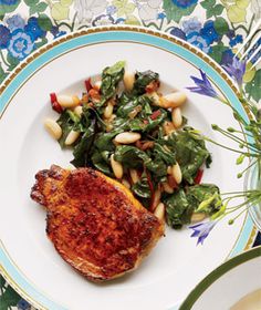 a white plate topped with meat and greens next to a bowl of sauce on a table