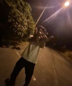 a young man is skateboarding down the street at night with his hands in the air