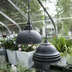 two hanging lights in a greenhouse filled with plants and potted planters on the side