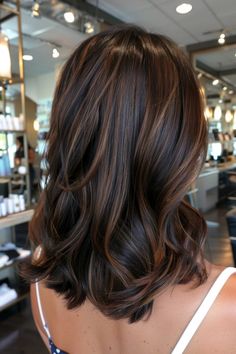 Person with wavy, shoulder-length brunette hair with caramel highlights in a salon.