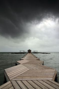 a wooden dock extending out into the ocean under a dark sky with storm clouds overhead