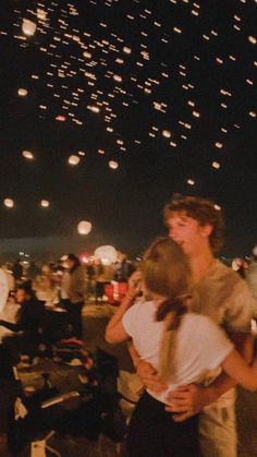 two people are hugging each other in front of the sky full of lights at night