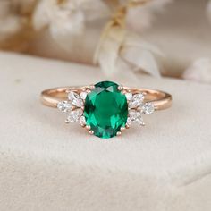 an oval cut emerald and diamond ring on top of a white cloth with flowers in the background