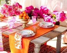 the table is set with pink flowers and oranges in vases on top of it