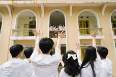 some people are standing in front of a building with their hands up to the sky