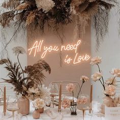 a table topped with vases filled with flowers next to a neon sign that says, all you need is love