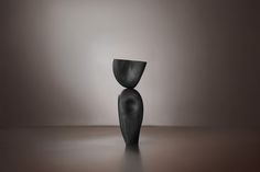 a black vase sitting on top of a table next to a white wall and floor