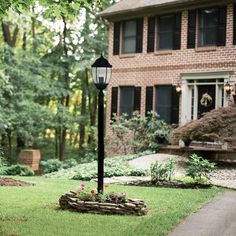 a lamp post in front of a house with flowers on the ground and grass around it