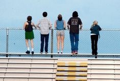 four people standing on the edge of a bleacher looking at something in the distance