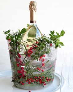 a bottle of wine sitting on top of an ice bucket filled with berries and greenery