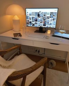 a desk with a computer and wine glasses on it, next to a lamp that is turned on