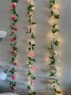 some pink flowers are hanging on the wall with lights around them and there is a lamp next to it