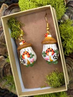 a pair of earrings in a box with moss