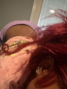 a woman with red hair laying on her stomach and wearing ear piercings in front of a window