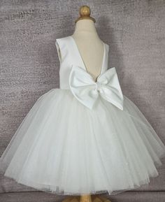 Elegant  glitter tulle flower girl dress for special occasions:  Off white flower girl dress.    Tulle  baby dress sewn by hand from the highest quality fabrics.   *Top of the  girl dress: satin, cotton inside.  *  Tulle skirt;   tulle, glitter tulle,  satin, lining with crinoline for fullness.   * detachable satin  bow *color off white *Knee  or tea length.   Dress comes in different sizes, please make sure to check the measurements below before placing your order. Available dresses according to customer dimensions White Tulle First Communion Dress With Tulle Skirt, Tulle Tutu Dress With Bow For Dress-up, Princess Tutu Dress With Bow For Wedding, Princess Style Wedding Tutu Dress With Bow, Princess Style Tutu Wedding Dress With Bow, White Princess Baptism Dress With Tulle Skirt, Elegant Tulle Tutu Dress With Bow, White Tulle Princess Dress For First Communion, Elegant Tulle Tutu Dress For Pageant