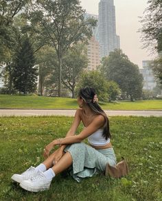 a woman sitting on the grass in front of a tall building with her legs crossed