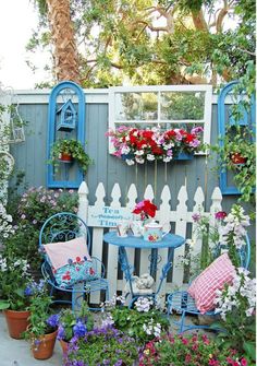 an outdoor garden with flowers and potted plants next to a white picketed fence