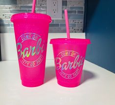 two pink plastic cups with straws sitting on a counter top next to each other