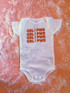 GRL PWR Baby Onesie Pink Cotton Onesie With Graphic Print, White Unisex Short Sleeve Onesie, Cute White Onesie With Graphic Print, Playful White Onesie With Name Print, Playful White Onesie With Letter Print, White Onesie With Graphic Print For Playwear, Fitted White Onesie With Graphic Print, Playful Orange Cotton Onesie, White Graphic Print Onesie For Playwear