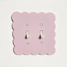 a pink scalloped light switch cover on a white wall with two lights in the middle