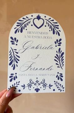 a person holding up a white and blue wedding card with an ornate design on it