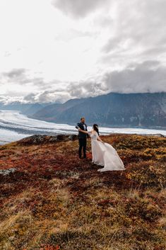 a man and woman standing on top of a grass covered hillside