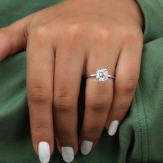 a woman's hand with a diamond ring on her left hand and white manicured nails