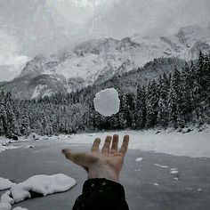 a person's hand reaching out towards the snow covered mountains and trees in the distance