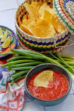 two baskets filled with chips and green beans next to another basket full of guacamole