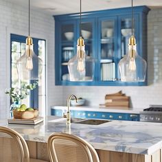 three lights hanging over a kitchen island with blue cabinets and marble counter tops in the background