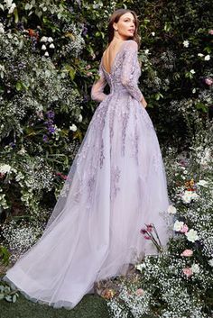 a woman standing in front of flowers wearing a purple dress with long sleeves and an open back