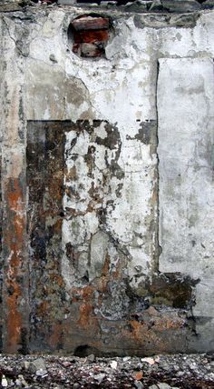 an old wall with peeling paint and some rust on the bottom half, along with a fire hydrant next to it