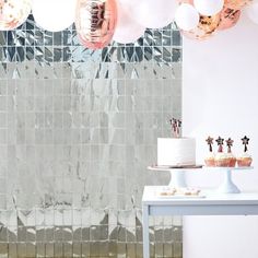 a white table topped with a cake next to a wall covered in pink and silver balloons